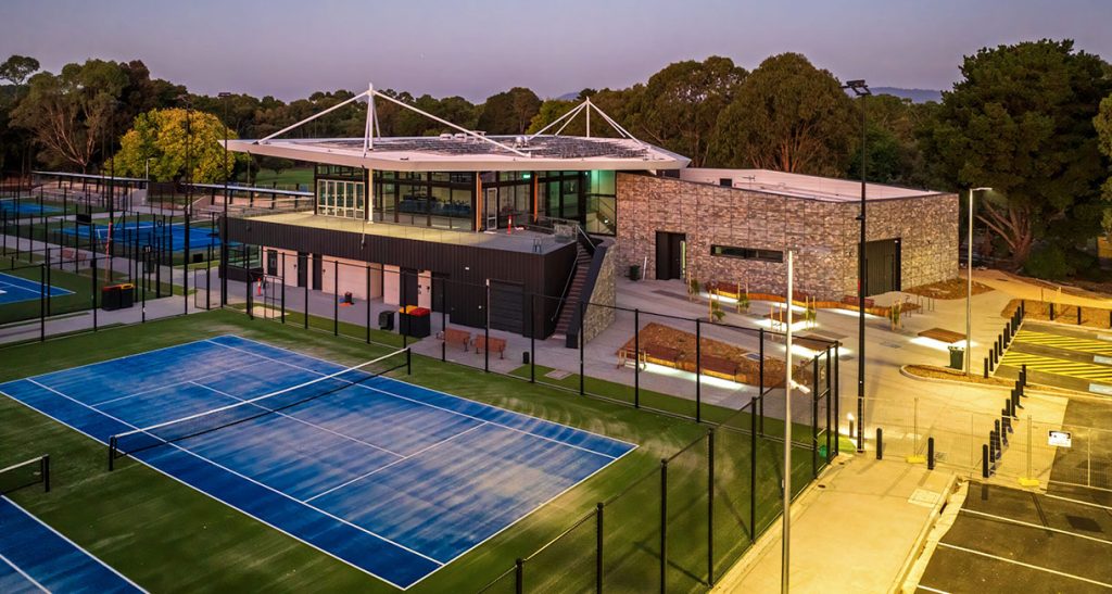 A dusk view of the tennis courts at Glen Waverly Sports Hub with the primary building lit up
